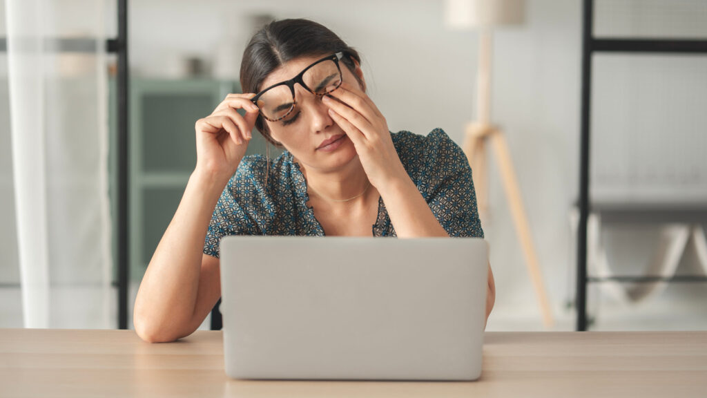 ノーパソの前で眠そうに目をこすっている女性